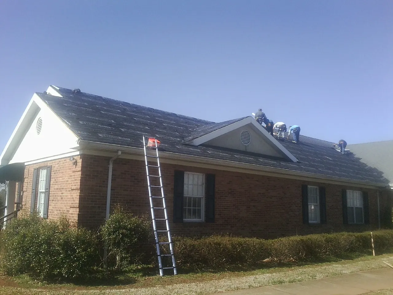 Crew tearing shingles off a brick ranch roof with a ladder set — Emergency Roof Repair work by our crew in Ft Mitchell