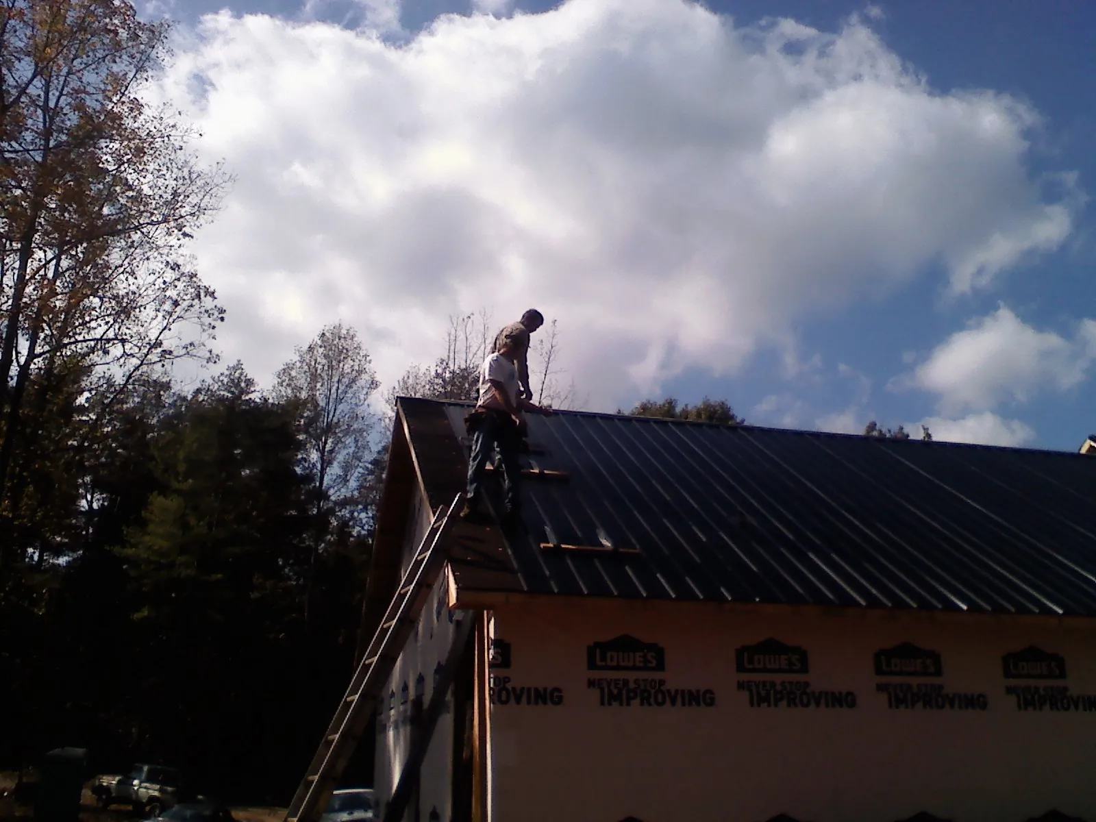 Roofer fastening dark metal panels high against a cloudy sky, from a Roof Inspection job in Ft Mitchell